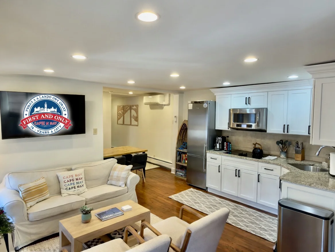 Modern open-concept living and kitchen with white cabinetry and granite counters in Cape May vacation rental