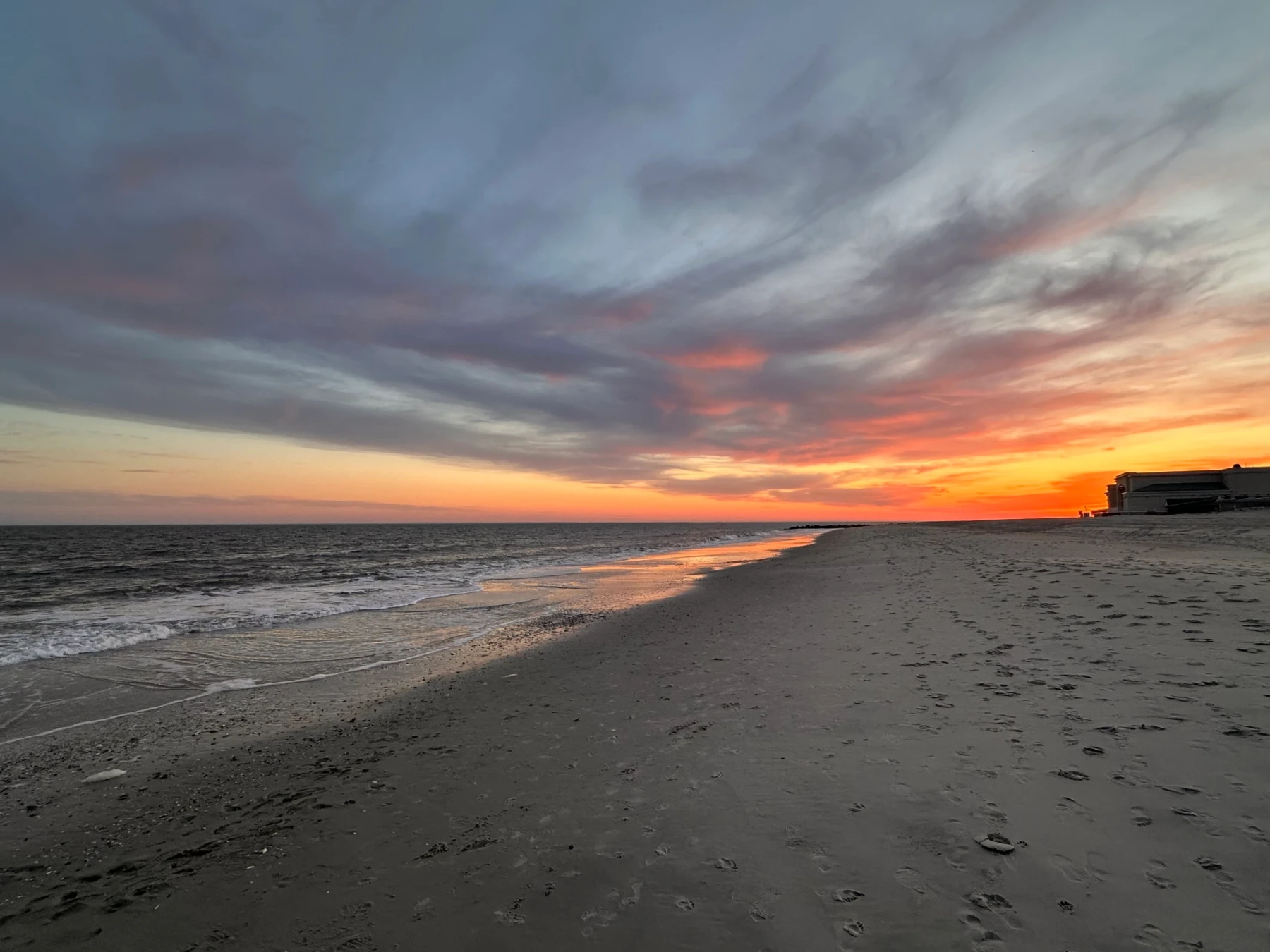 Golden hour beach sunset with vibrant orange and gold hues reflecting on wet sand and calm ocean waters in Cape May